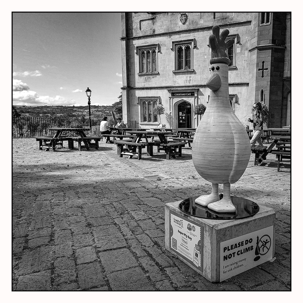 A small statue of Feathers McGraw (a penguin disguised as a chicken) from the Wallace & Gromit series sits amid a cafe scene with a small section of the Ashton Estate viewable in the background.