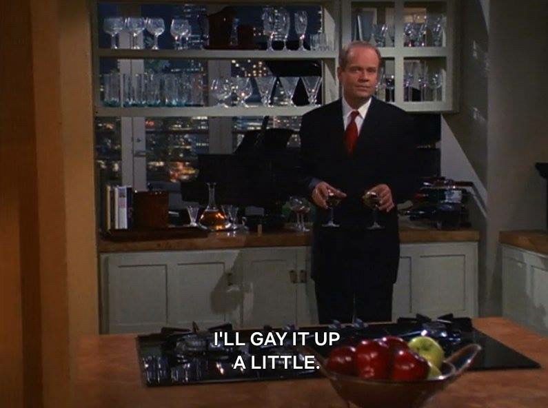 Frasier Crane, in his kitchen in front of a basket of apples of mixed colors and holding two small glasses of wine while standing in front of his decanter set and behind that the piano next to the window-doors to the balcony where you can see Godzilla attacking Seattle, saying “I’ll gay it up a little”