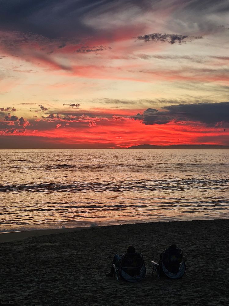 View of a ocean beach at sunset. The sky is red and grey.