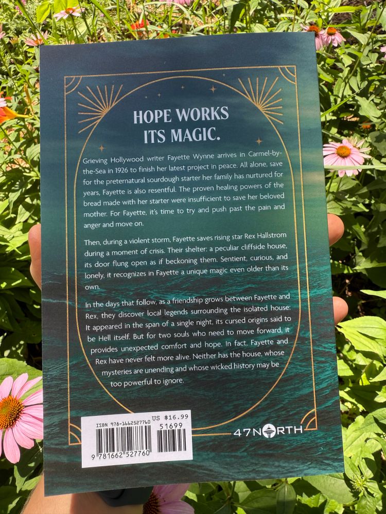 A green and blue book cover is held against a bed of blooming coneflowers.