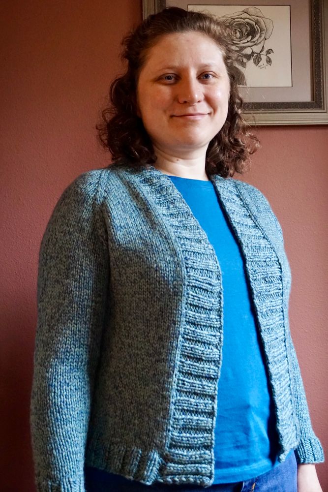 Photo of me wearing the cardigan from the front and turned slightly away. The cardigan front is open over a tee shirt of closely coordinating dark teal.