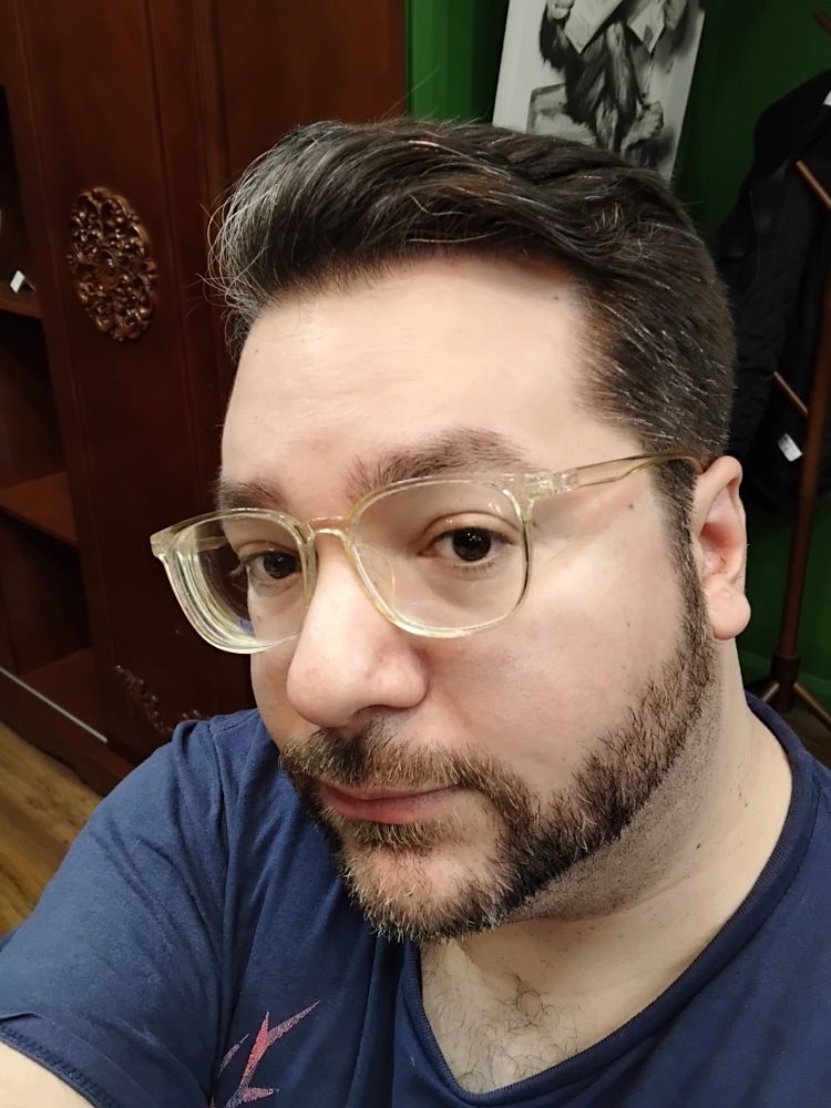 Serge is a Caucasian person with short brown hair, a beard and moustache. He wears clear glasses and a blue t-shirt 