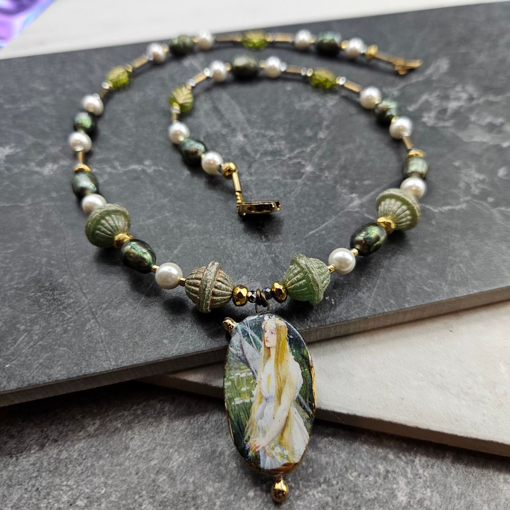 An ornate gold and pearl necklace with a white fairy focal in sage green