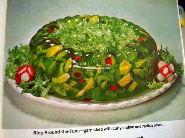 cursed 50s jello salad called Ring-around-the-tuna (presumably some kind of lime jello with tuna salad inside, as well as visible chunks of vegetables like olives and yellow peppers) garnished with curly endive and radish roses