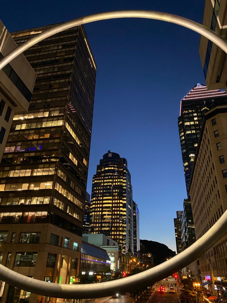 Skyscrapers and the edge of Mont Royal, framed through the gigantic ring mounted atop Place Ville Marie in Montreal