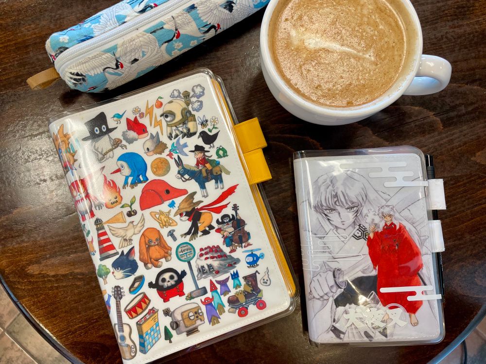 A photo of two planners, a pen case, and a latte sitting on a cafe table.