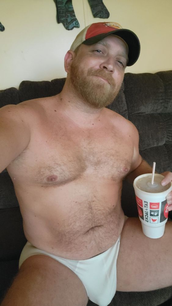 Guy sitting in a couch in his tighty whities and a cap
