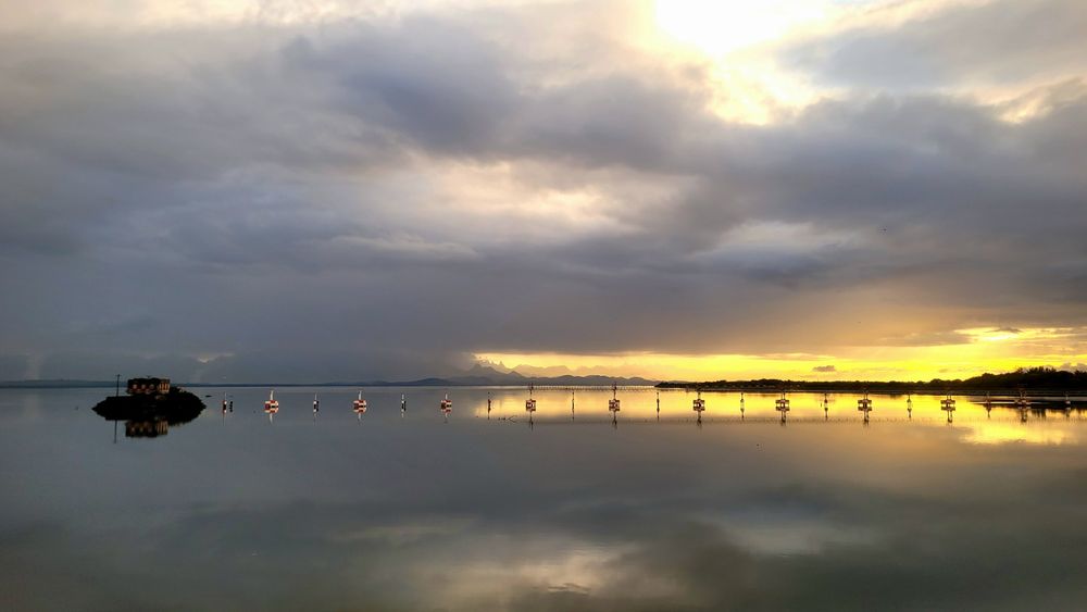 Baía de Guanabara refletindo o céu cheio de nuvens cinza e um trecho iluminando de amarelo pelo Sol 