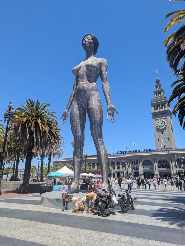 The Giant Woman statue, with the Ferry Building and some palm trees behind it