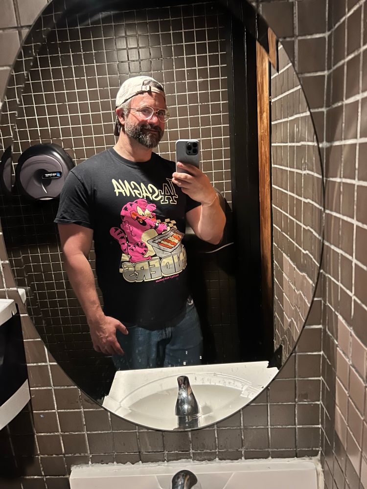 Me in a bathroom mirror selfie, backwards hat and aviator glasses, beard looks nice in the dim light
