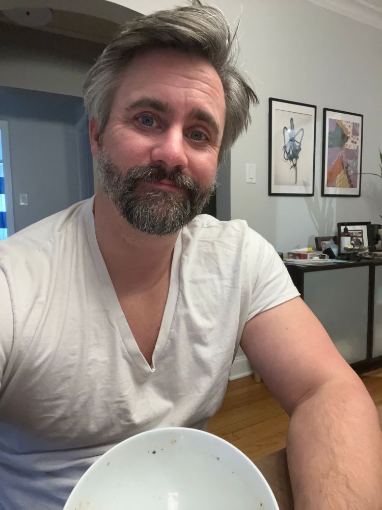 Mike in a white v-neck shirt with an empty soup bowl in front of him. 