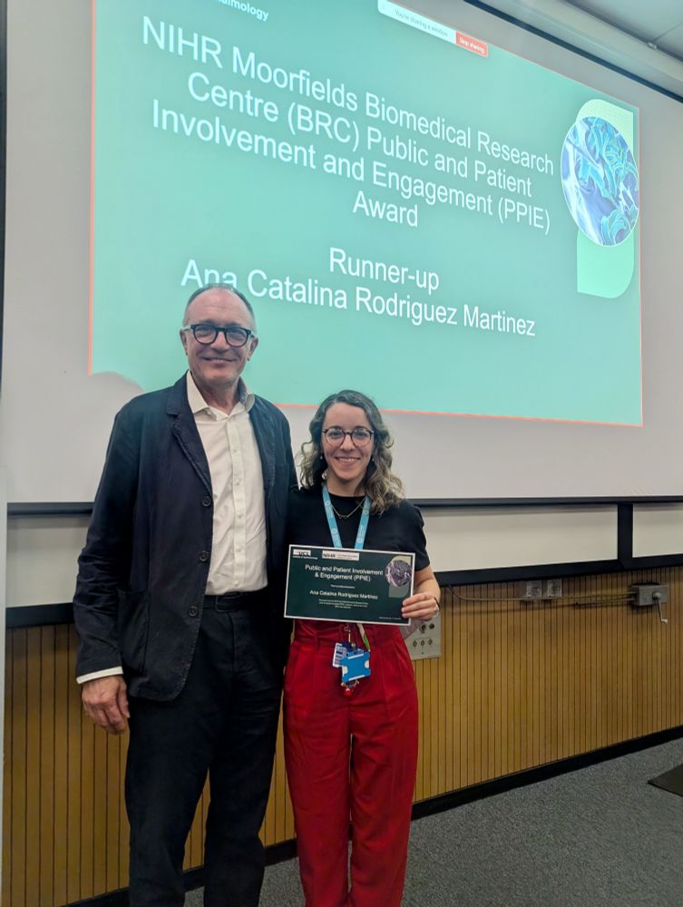 Two people standing in front of a presentation screen. The screen displays the text 'NIHR Moorfields Biomedical Research Centre (BRC) Public and Patient Involvement and Engagement (PPIE) Award Runner-up Ana Catalina Rodriguez Martinez.' One person is holding a certificate with similar text. 
