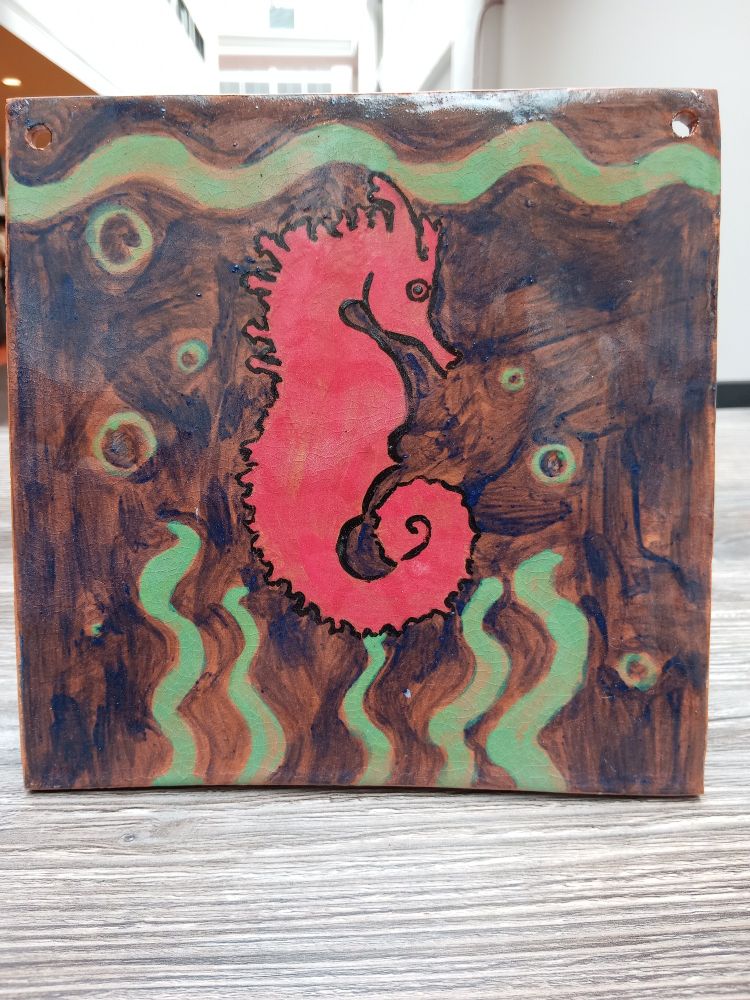 A ceramic tile with a bright red sea horse in the middle on a blue(ish) background