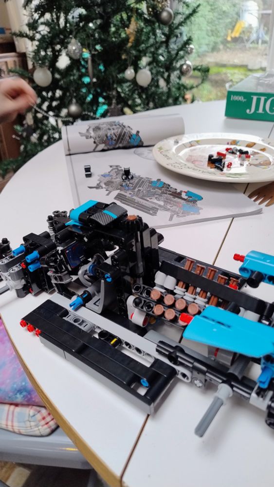 Partially built Technic Lego model on a white table with a Christmas tree in the background.