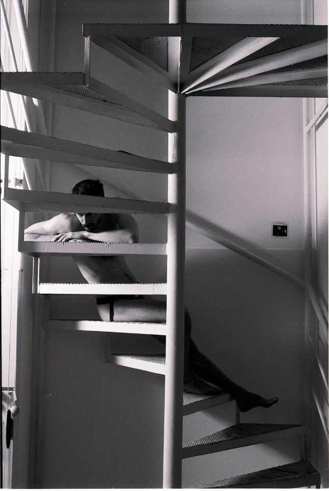 Black and white photo of man in underwear sprawling on spiral staircase