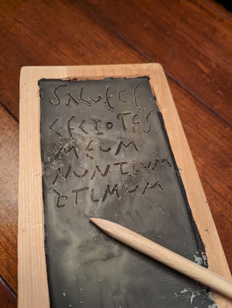 Imago styli et tabulae ceratae, quae nuntium "Salvete Lectores Meum Primum Nuntium" in facie sua habet
