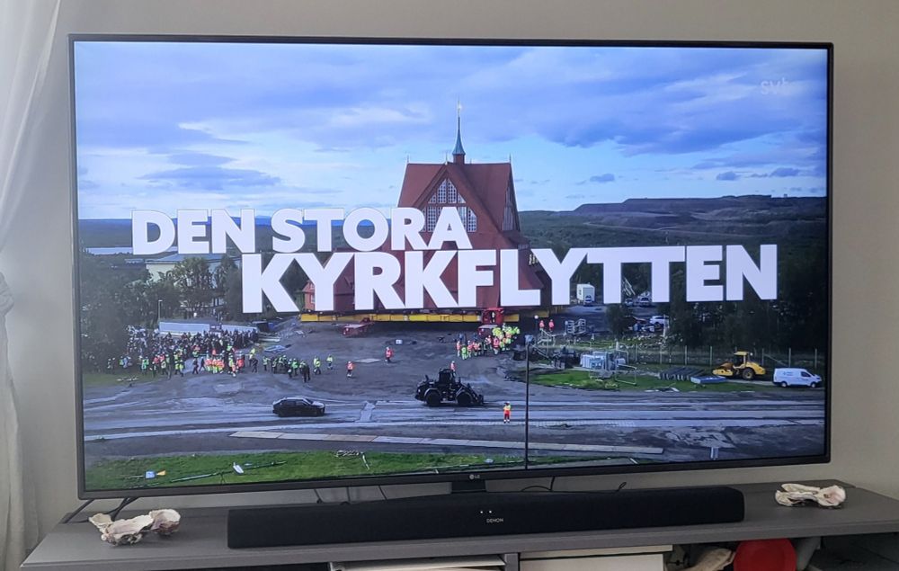 Bild på en tv-skärm som visa programmet Den stora kyrkflytten på SVT. I bakgrunden Kiruna kyrka, framför den stor vit text med namnet på programmet.