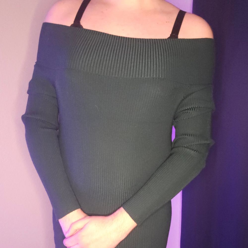 A pic of nova in a tight green dress with black bra straps on her shoulders. She has her hands infront of her over her groin
