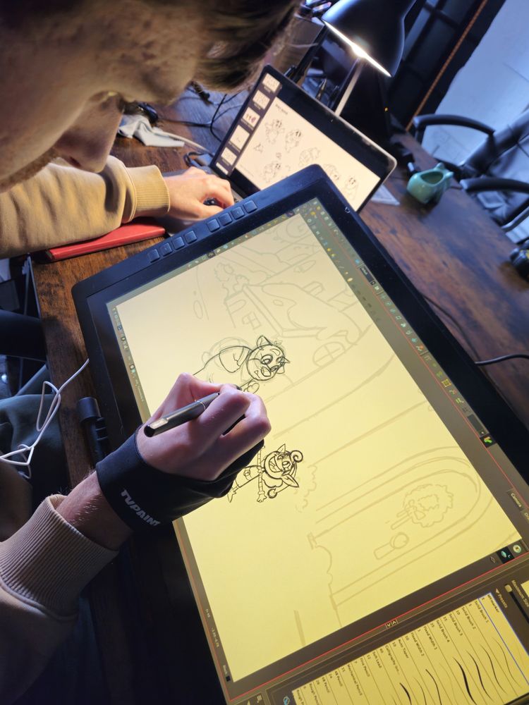 A close-up, over the shoulder shot of animator Nathan J. Hill sketching a Christmas scene featuring Bucky the Unicorn Bear and Tappy, on a large digital tablet.