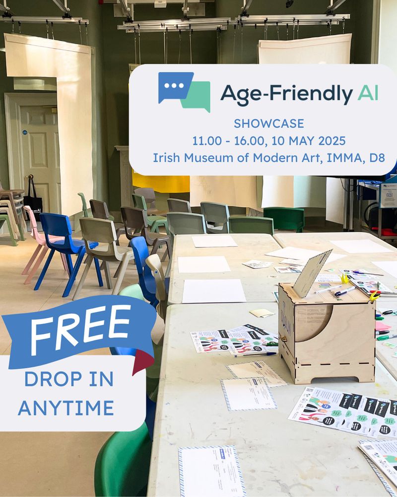 a bright and airy room, within the Irish Museum of Modern Art (IMMA) in Dublin, set up for an "Age-Friendly AI Showcase" on May 10, 2025. The foreground features several light-colored tables scattered with papers, colorful stickers, pens, and a small, light wood voting box. Various chairs in pastel shades of pink, blue, and light green are arranged around the tables, suggesting an interactive workshop or drop-in event. A banner in the bottom left corner proclaims "FREE DROP IN ANYTIME" in bold white letters against a blue background with a red ribbon detail. In the midground, a white sign with rounded corners clearly displays "Age-Friendly AI SHOWCASE" in a modern font, along with the event time (11:00 - 16:00) and location (Irish Museum of Modern Art, IMMA, D8). The background shows the high ceilings and muted green walls of what is a workshop space within the museum, with hanging white fabric panels and some storage or equipment visible in the periphery. The overall impression is of a welcoming and accessible event focused on artificial intelligence for older adults.