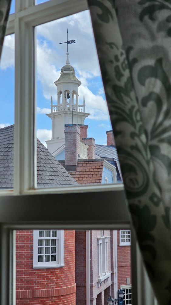 A view of a colonial building outside a window with curtains.