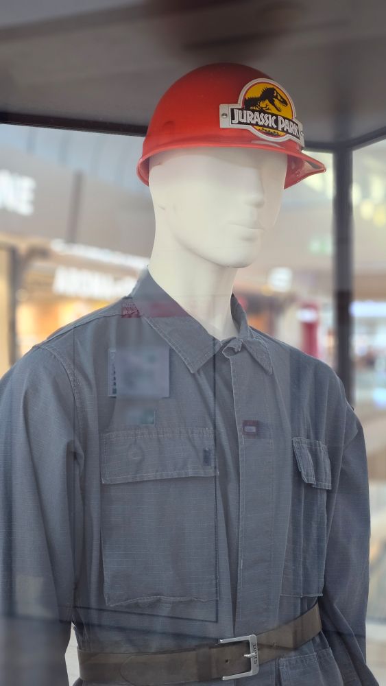 Blue overalls and a red hard hat bearing the Jurassic Park logo, on a mannequin.