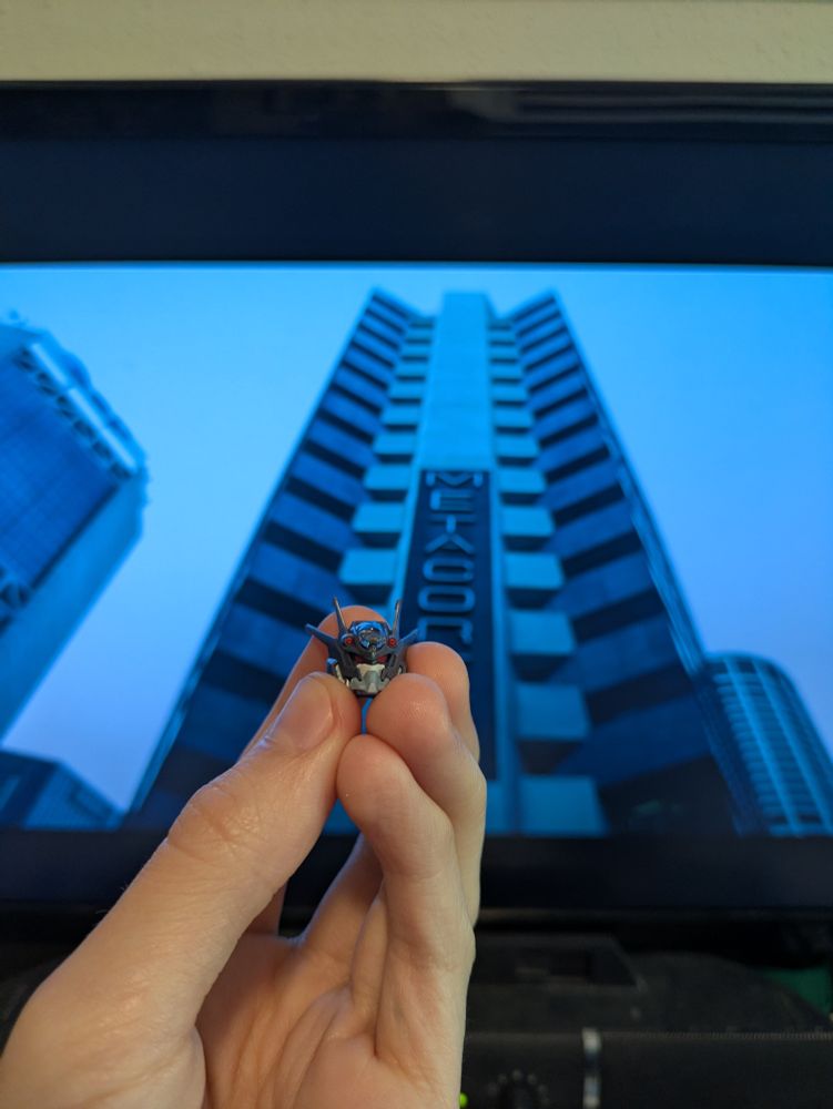 Gundam Pharact's head held up in front of a screen displaying a shot from The Matrix.