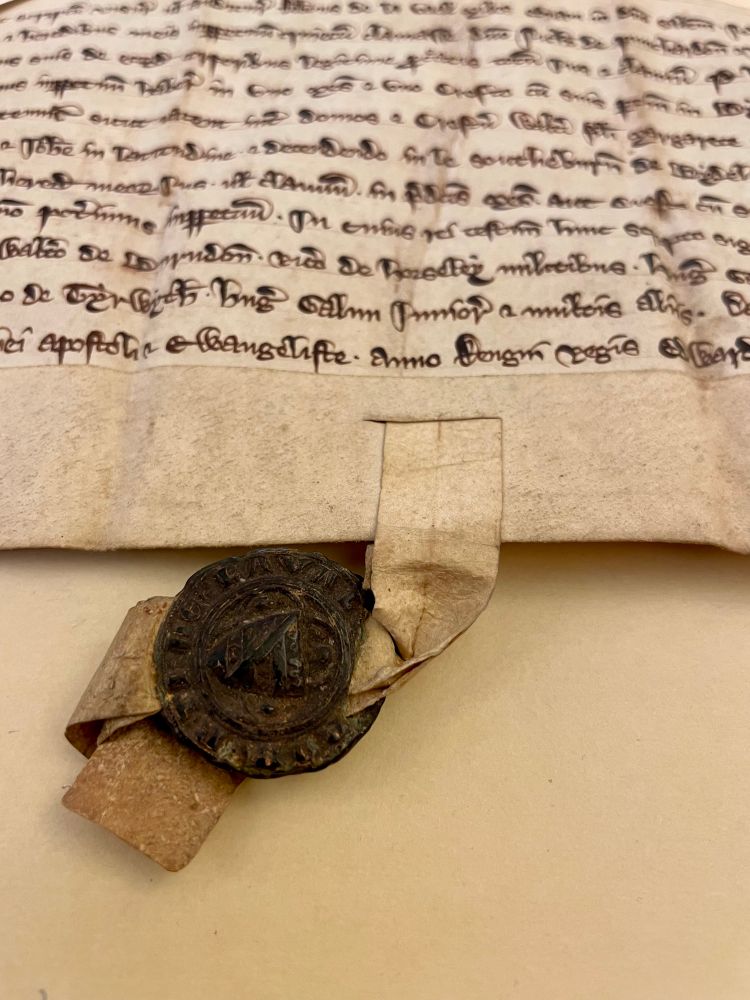 A medieval document with one or two lines of handwriting visible at top, dark colored wax seal attached to a strip of parchment at the bottom of the document 