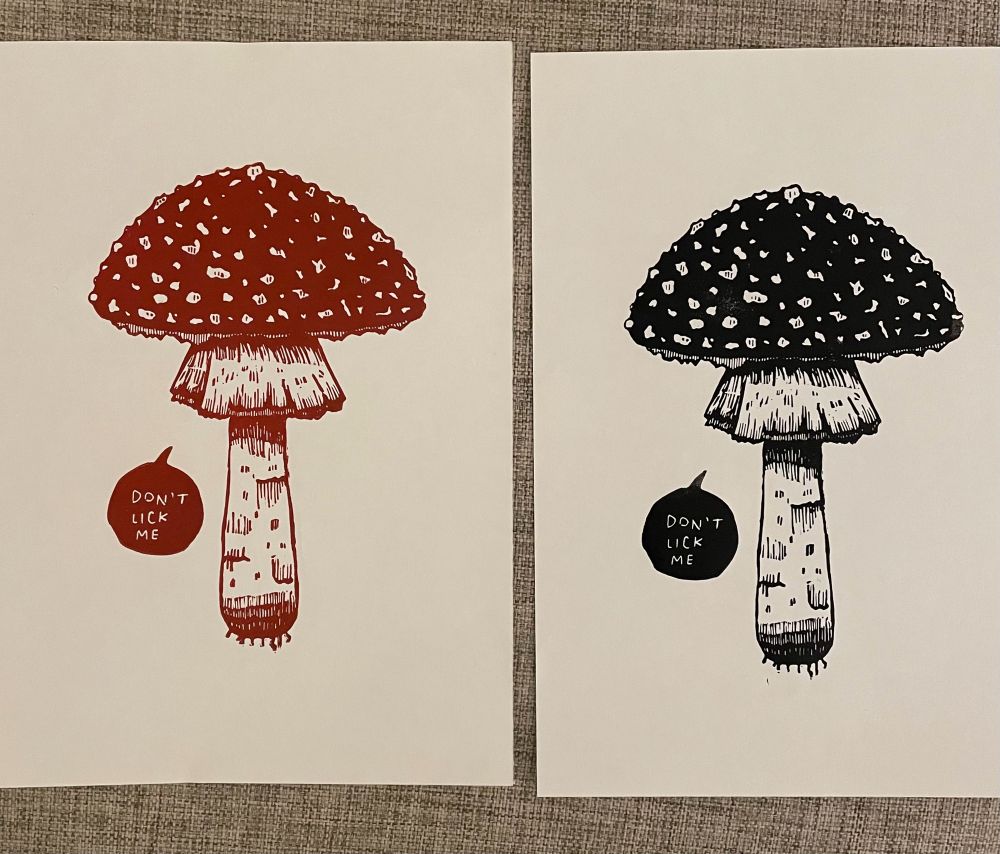 Two identical linocut prints of Fly Atarix mushrooms with white spots on the cap. Left: red and white. Right: black and white. 