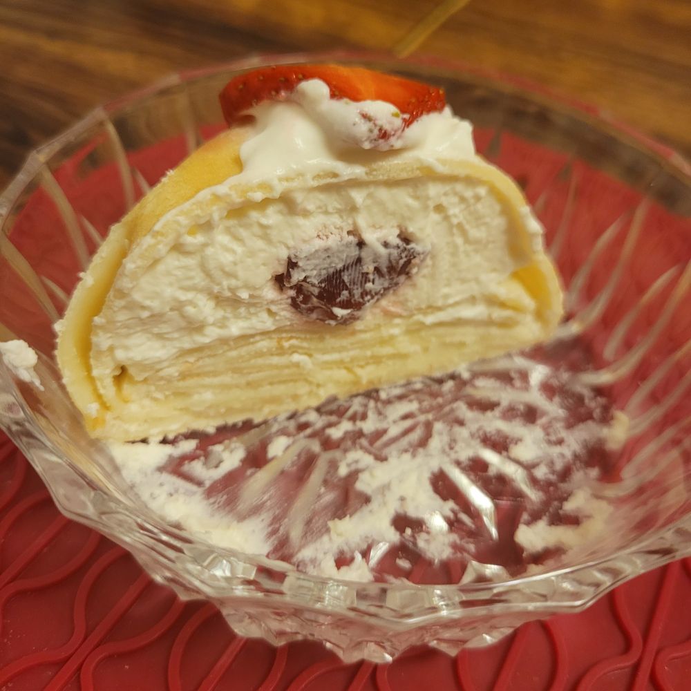 Cross section of a crepe pouch in a glass bowl. It is filled with whipped cream with a red strawberry in the centre. 