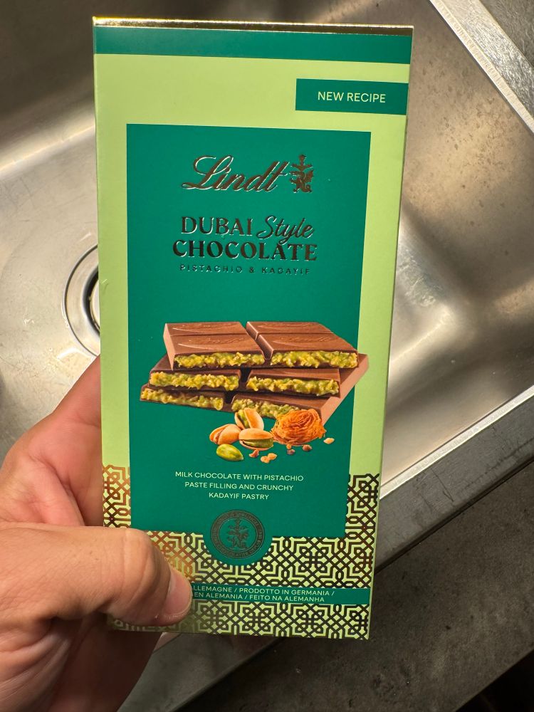 Foto de uma barra de chocolate da lindt verde, de chocolate com pistache escrito “Duvai Style Chocolate”