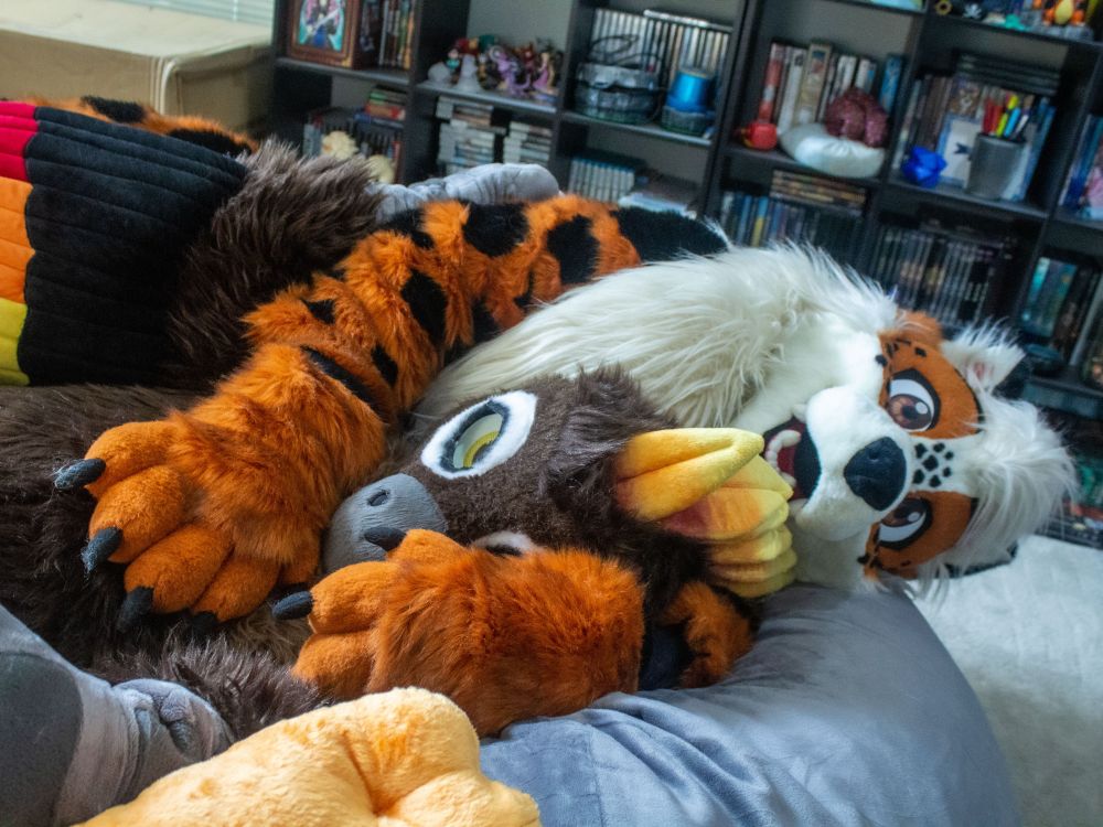 An arcanine and phoenix fursuit cuddling in a beanbag together.