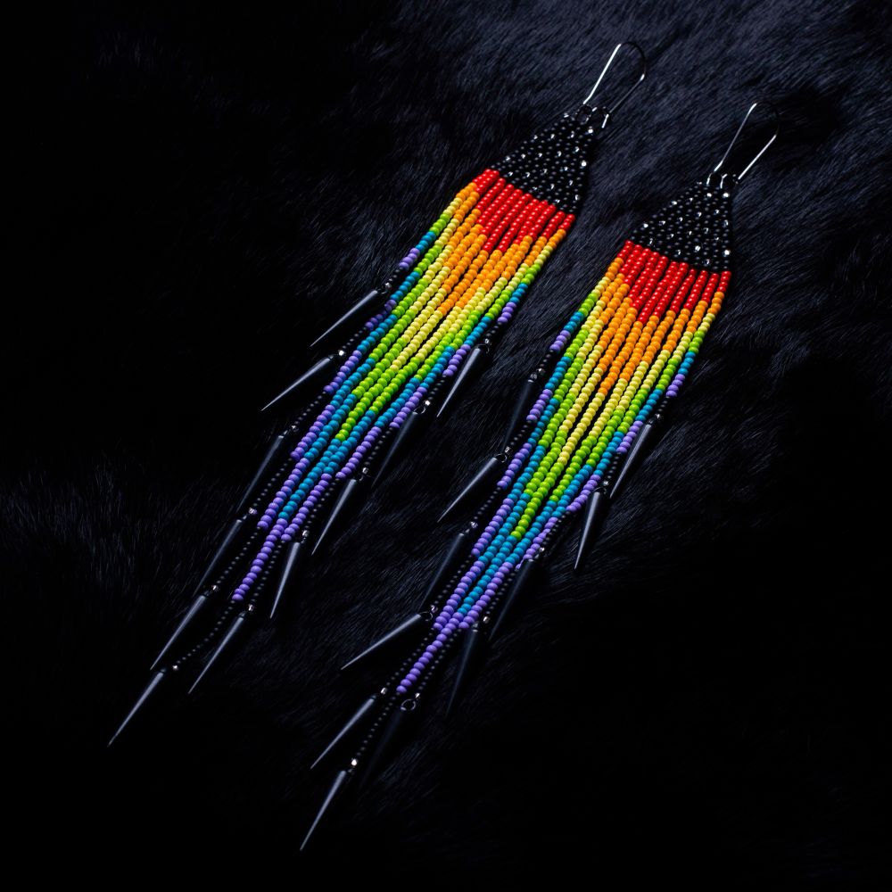 Fringe earrings on a black backdrop. Top triangle of the earrings represent the stars. The fringe is a rainbow blend from red to purple, representing the rainbow road. With black spikes at the ends. Backdrop is black rabbit fur.