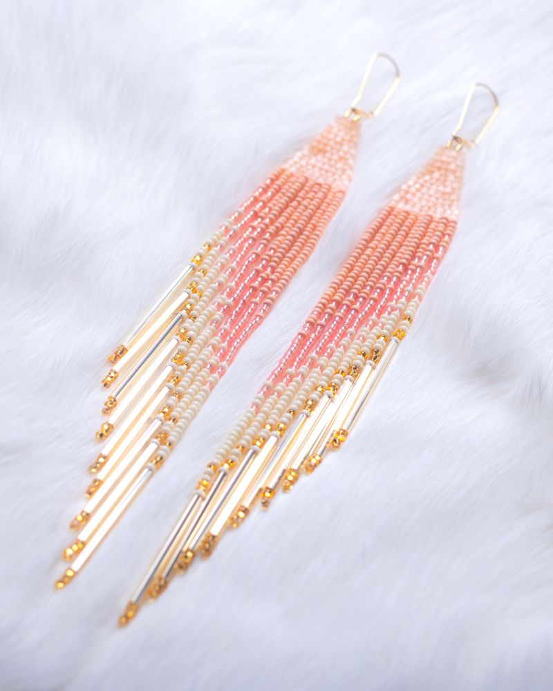 peach fringe beaded earrings blended into cream. with gold bugle beads at the end. shaped like feathers. on a white rabbit fur backdrop.