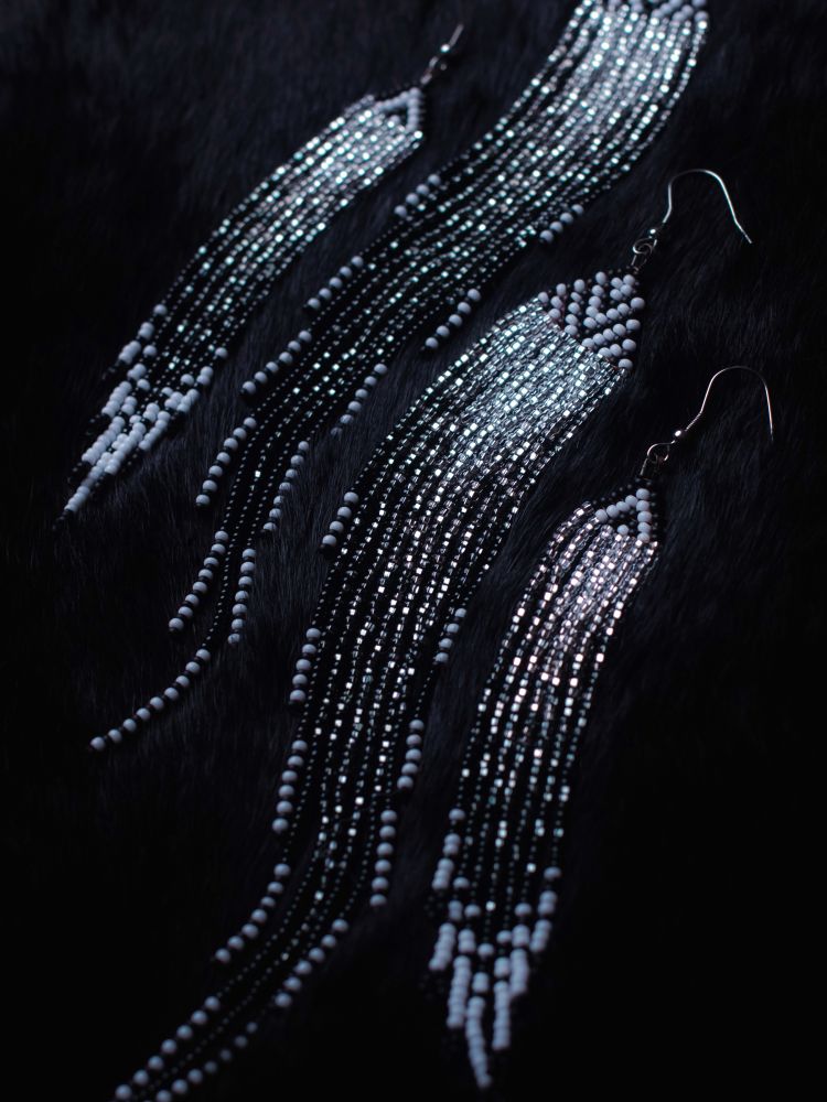 Monochrome Black, Silver, White sparkly beaded fringe earrings. Middle are a large pair with a black and white lined triangle on top, blended white to black for the fringe. With white and black repeated ends. Smaller fringe earrings are on the outside, with similar designs. Laid on a black fur backdrop.