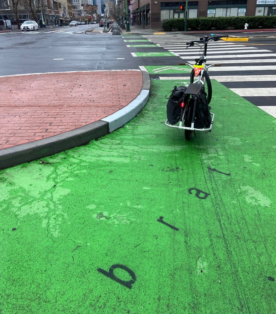 “brat” stencil on green bike lane in a protected intersection 