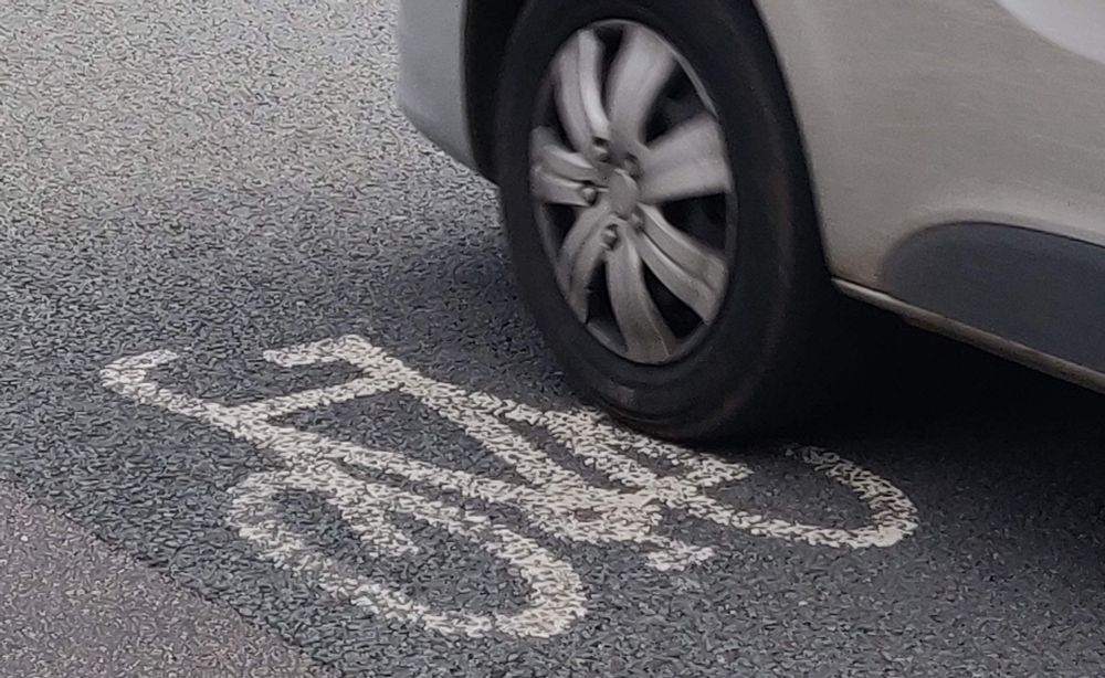 The wheel of a vehicle drives over a painted bike on the road where cyclists are supposed to ride, it is a poignant reminder that paint is not infrastructure.