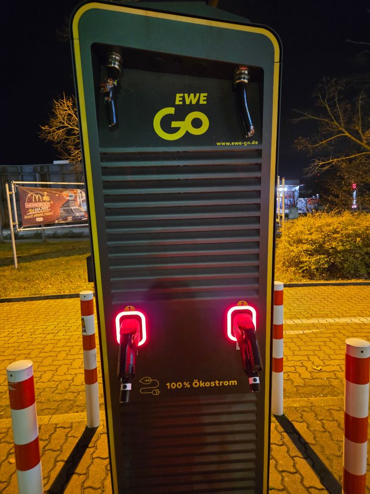 Eine EWEGo Ladestation für E-Autos. Die beiden Ladekabel sind abgeschnitten und gestohlen worden. Die Ladestation leuchtet rot und zeigt dass sie nicht betriebsbereit ist.