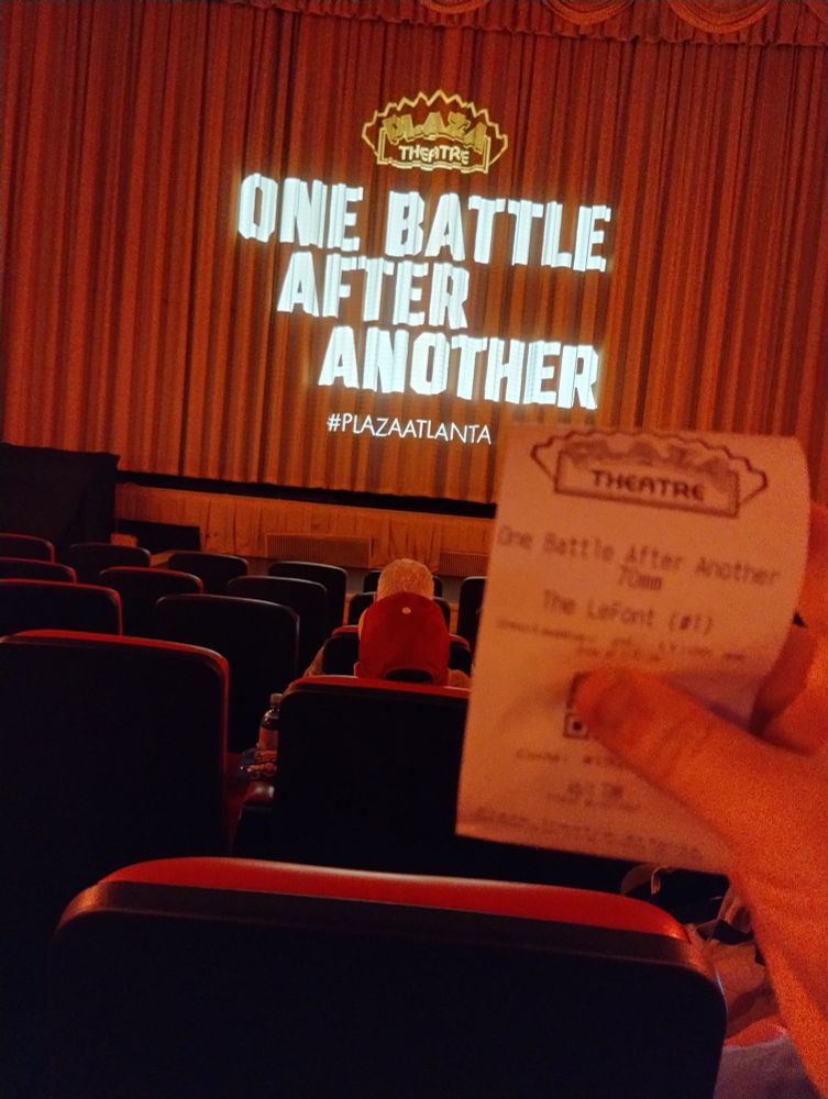 Me in the theater waiting for One Battle After Another, the title is projected on the curtains while I hold up my ticket 