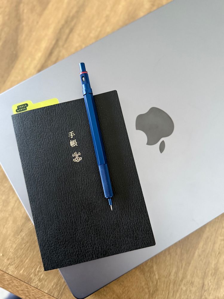 Wooden table with macbook pro, hobonichi techno planner, and mechanical pencil. 