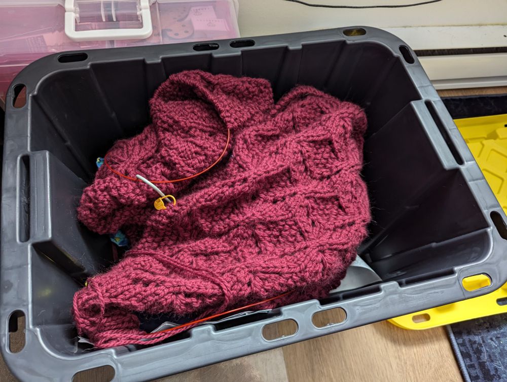 Deep maroon knitted blanket, with diamond textured patterns, in a utility box, yellow lid to the side.