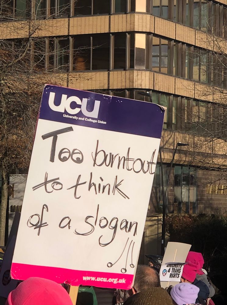 A UCU placard that reads “too burnt out to think of a slogan” in front of a tower block and another placard reading “trade unionists for trans rights”