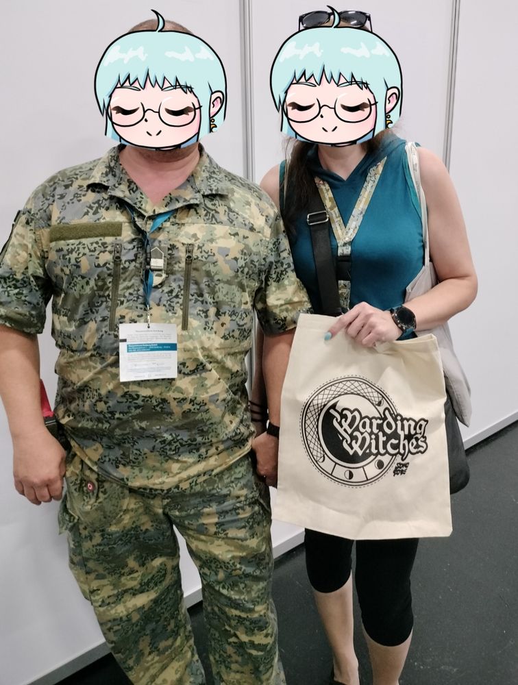 A couple posing for a photo with a Warding Witches tote bag