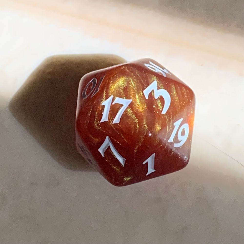 A caramel coloured and sparkly twenty sided dice is half sitting in a sunbeam. 