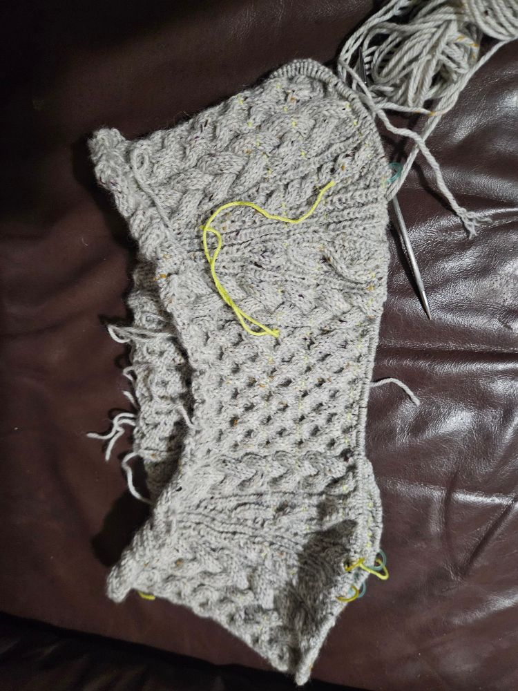 The yoke of a sweater in speckled gray. Different sections have different cable patterns on them. 