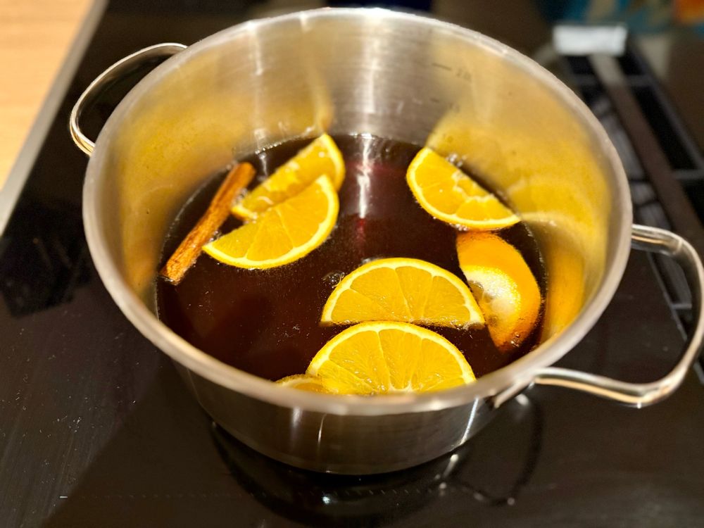 In einem Kochtopf mit brauner Flüssigkeit schwimmen Orangenscheiben und eine Zimtstange