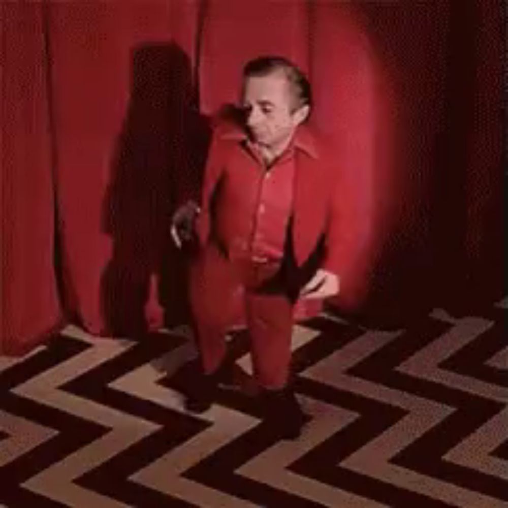 a very small man in a red suit is dancing on a zigzag floor .