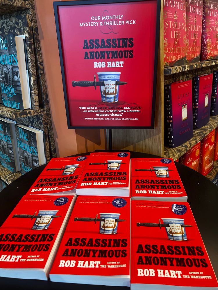 A table full of copies of the book Assassins Anonymous by Rob Hart