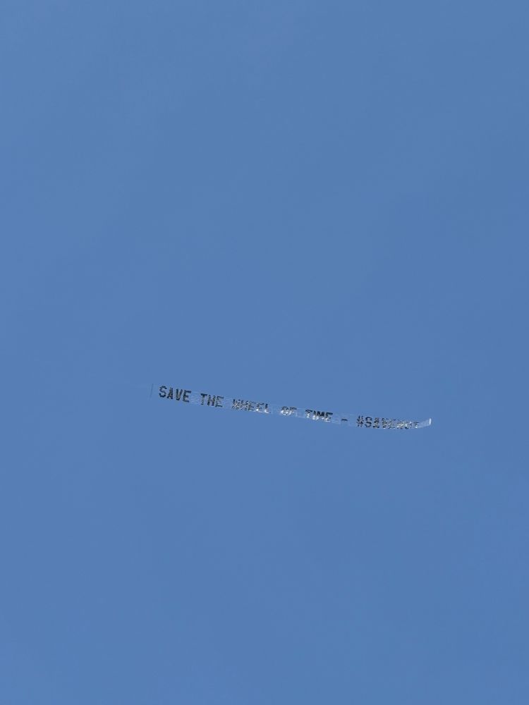 The banner behind a plane reads "save the wheel of time - #savewot" 