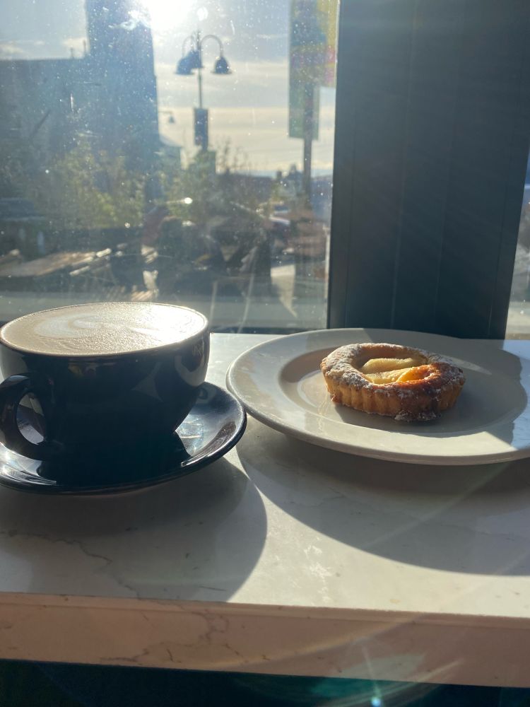 The view from a stool in the cafe, coffee and pear tart on the counter, the church bathed in sunshine 